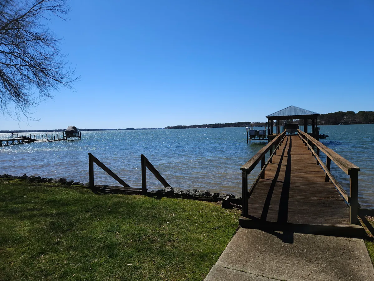 A serene view of a dock extending into calm lake waters, with a boathouse and green grass visible. The tranquil scene encourages fishing, kayaking, and picnicking, with the expansive lake providing a sense of endless adventure.
