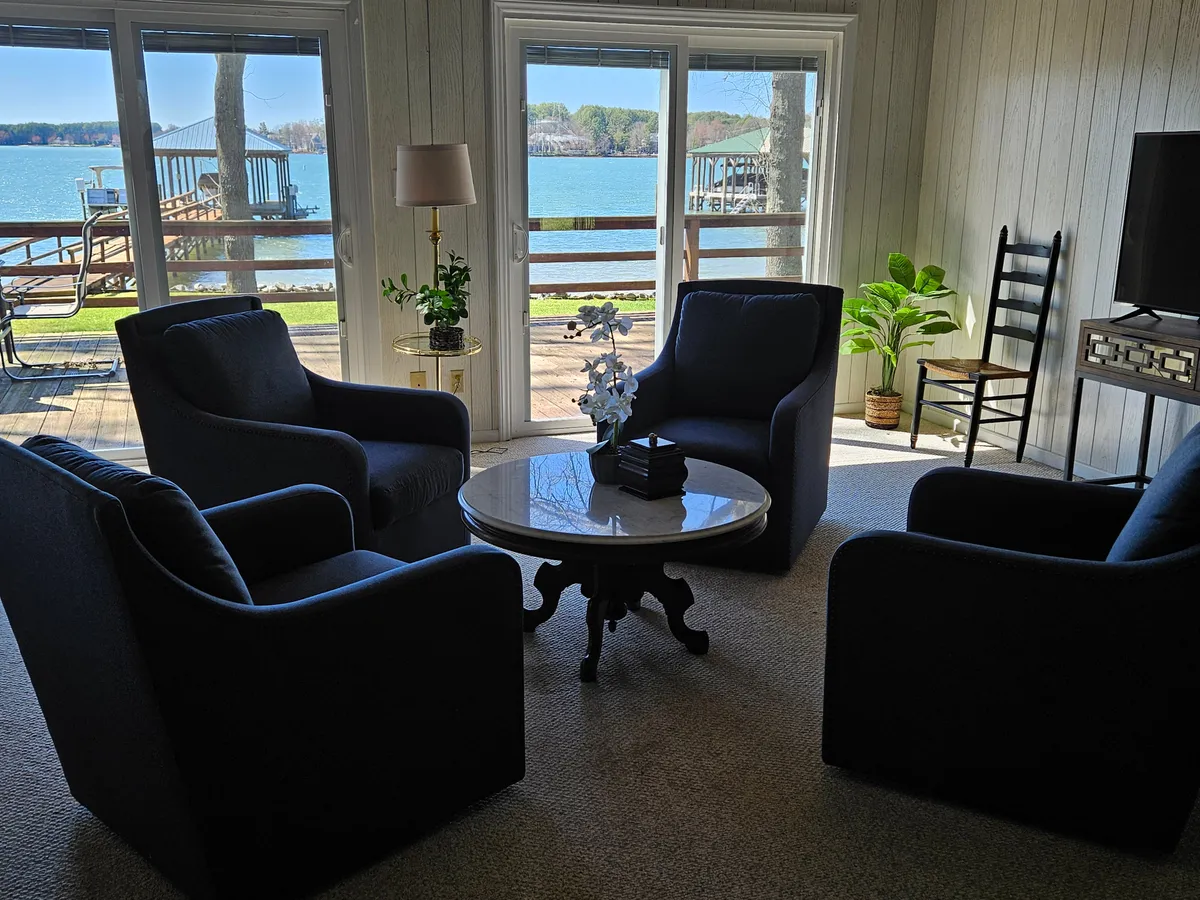 Spacious seating areas arranged around a coffee table are set in front of expansive windows that frame stunning lake views. Indoor plants and decorative touches add to the tranquil, welcoming atmosphere, while natural light floods the space.