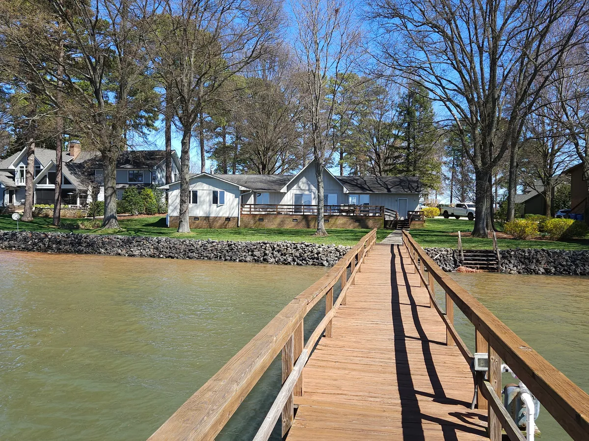 An inviting view of the waterfront house framed by trees, with a wooden dock extending into the calm lake. The landscaped surroundings and spacious dock evoke a peaceful yet social atmosphere, ideal for group relaxation and activities.