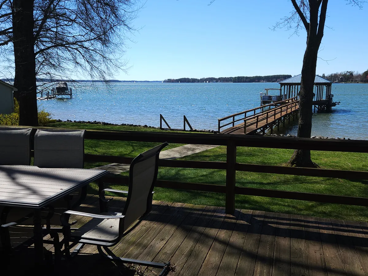 A tranquil lakeside view with a dock and comfortable outdoor seating arranged to take full advantage of the water scenery. The peaceful setting highlights the allure of morning coffee or evening relaxation, with the deck’s proximity to the water drawing the outdoors in.