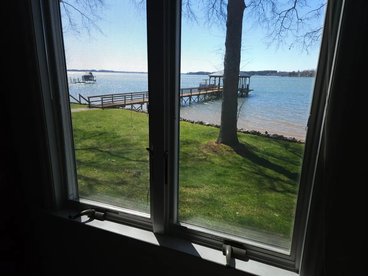 A wide view featuring a dock extending into the lake, bordered by a green lawn and mature tree. The tranquil mood is ideal for morning coffee, sunset viewing, or leisurely outdoor activities along the water’s edge.