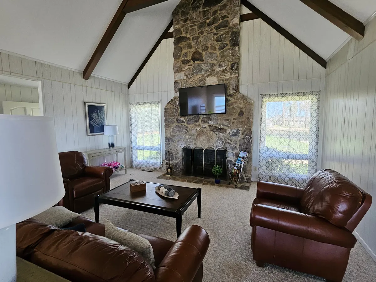 A cozy stone fireplace forms the centerpiece of the great room, flanked by leather armchairs and a central coffee table. The arrangement encourages conversation, relaxation, and shared activities such as games or watching TV. The room exudes a warm, inviting atmosphere perfect for gatherings.