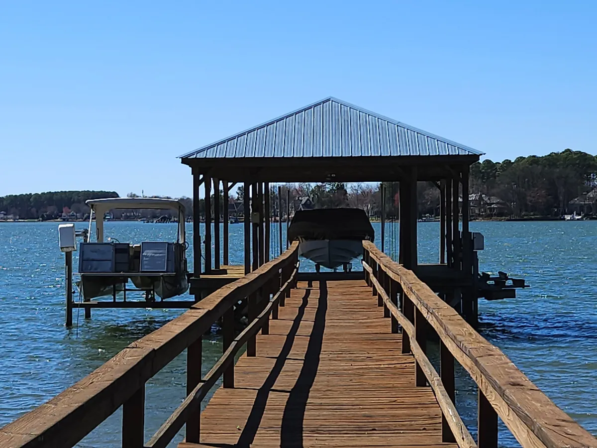 This exterior image features a spacious wooden dock extending over the water, with a boathouse and several boats moored nearby. Gentle ripples on the lake surface reflect the serene atmosphere, and the wide dock provides ample space for gatherings and relaxation by the water.