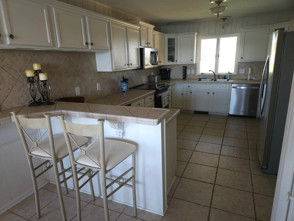 This image showcases a bright, open kitchen centered around a generous island with seating. Stainless steel appliances line the space, and natural light streams in through a window, making the kitchen feel both functional and welcoming. The seating at the island suggests an inviting space for casual meals or for friends and family to gather while cooking.
