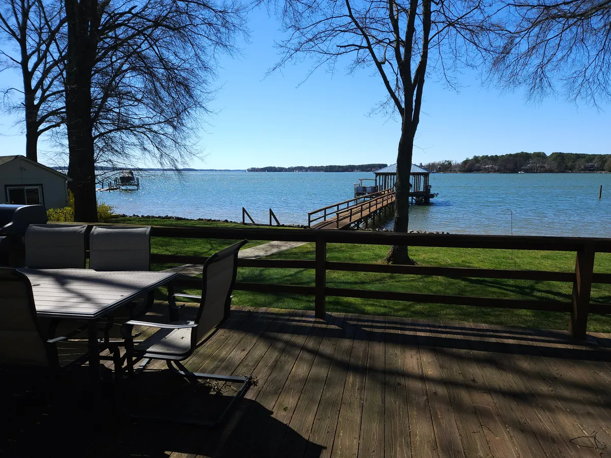 A tranquil view of the lake framed by a dock and comfortable outdoor seating shaded by trees. The scene invites relaxation and group conversation while enjoying peaceful water views and the natural beauty surrounding the property.
