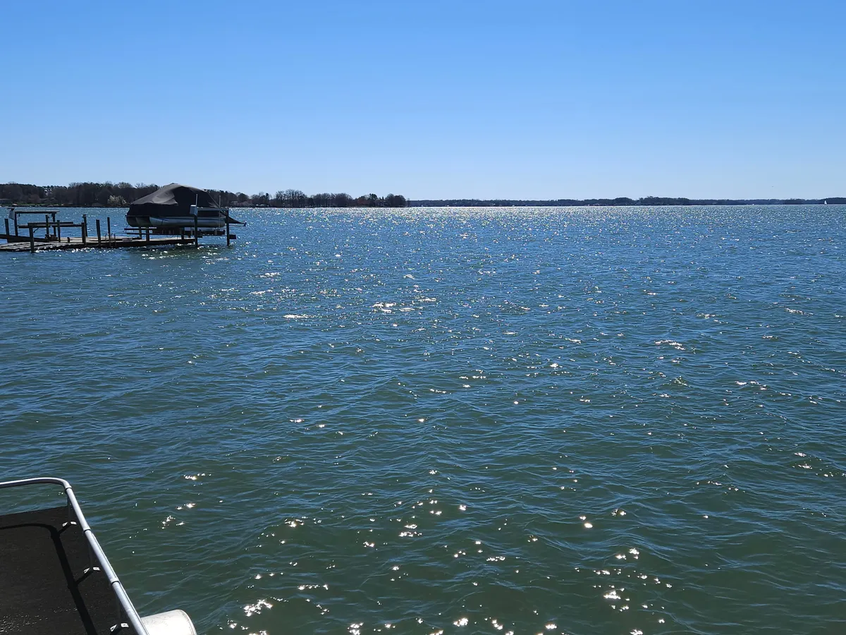 A peaceful lakeside view featuring sparkling water, a distant shoreline, and a boathouse perched on a pier. The setting is ideal for fishing, boating, and relaxed picnics, especially at sunset.