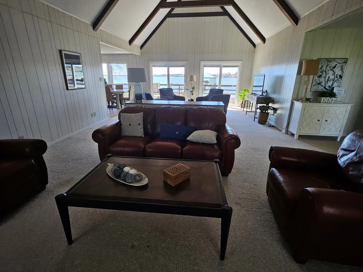 A comfortable leather sofa faces a coffee table and large windows that look out onto the water. The room feels cozy and welcoming, ideal for relaxing, family movie nights, or casual gatherings with friends.